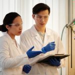 Illustrative photograph: Researchers discussing data in a laboratory setting, wearing safety gear and blue gloves.